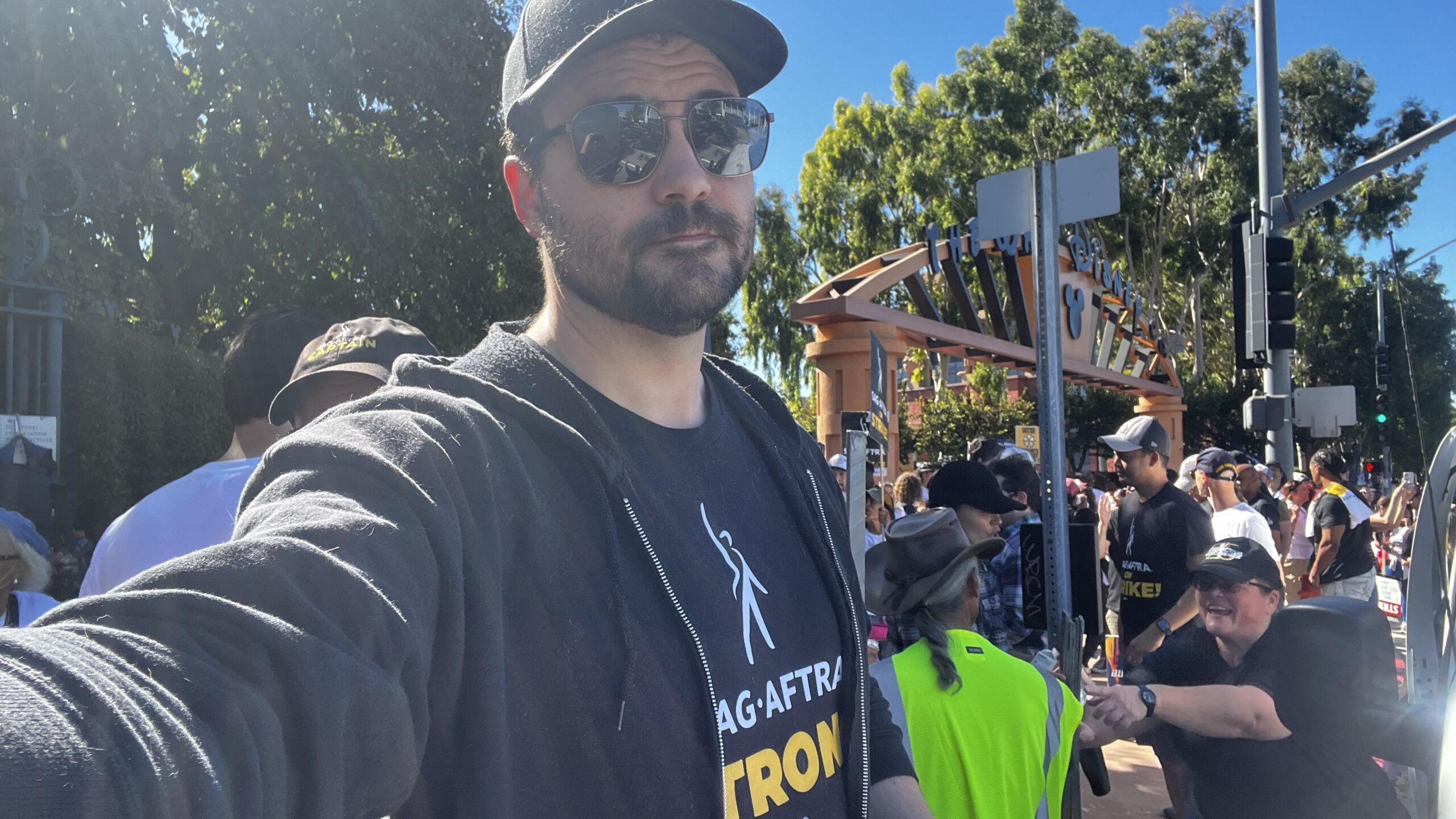 Person at protest wearing a black tee shirt that reads "SAG-AFTRA Strong", taking a selfie