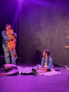 Two performers on stage with purple lighting.