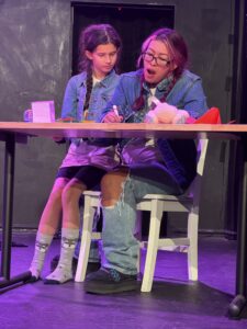 Two people in denim at a table on stage.